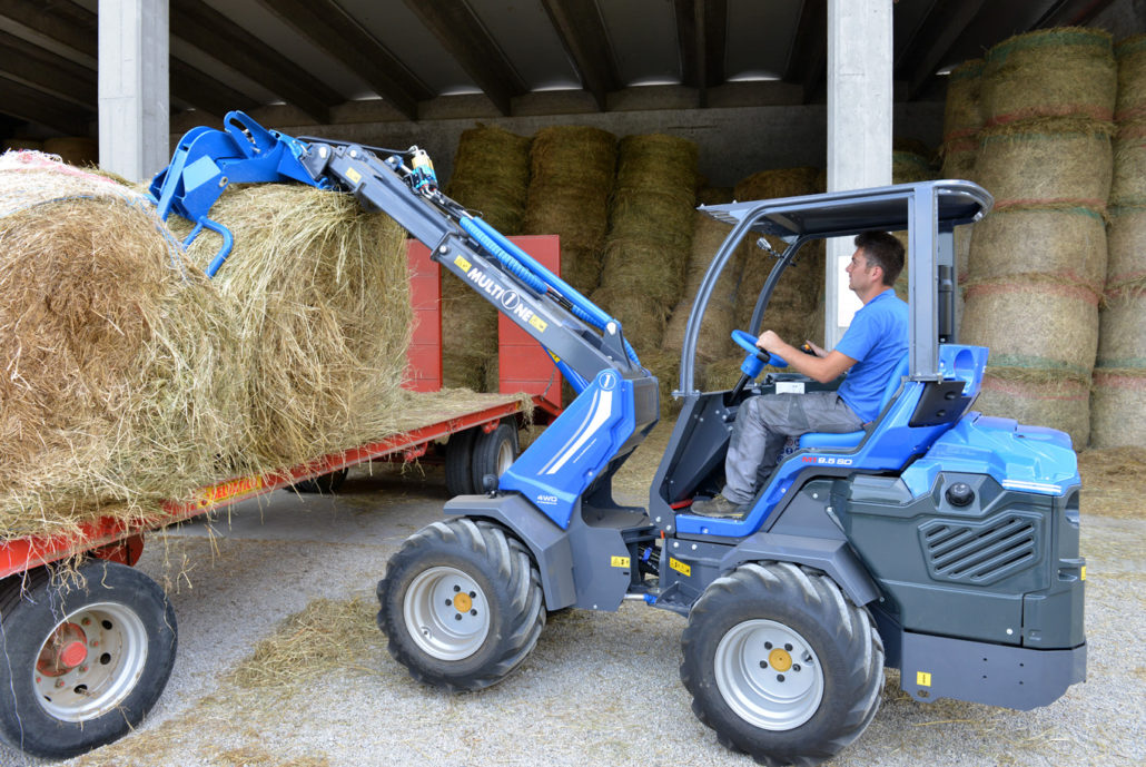 man driving a mini loader and using an hay bale grapple to grab a hay bale