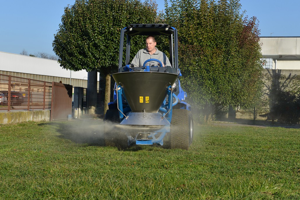 a man drive a salt and sand spreader on a grass lawn during a sunny day