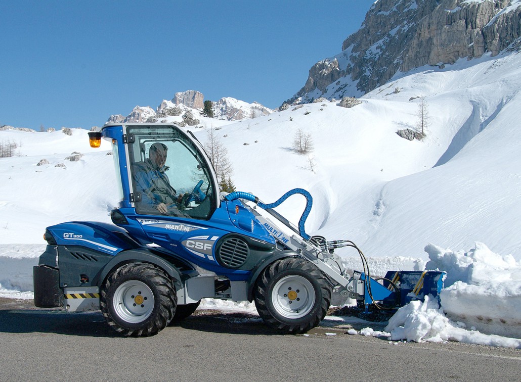snow blade cleaning the side of a street among the mountains